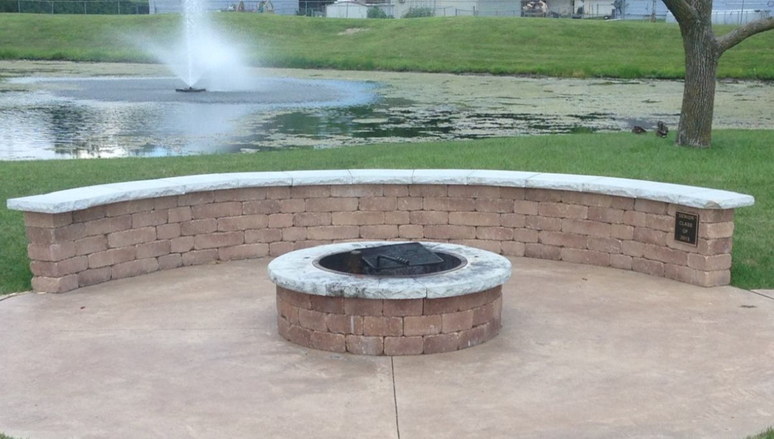 Seating wall installed by fire pit and water on landscaping in Ankeny, IA.