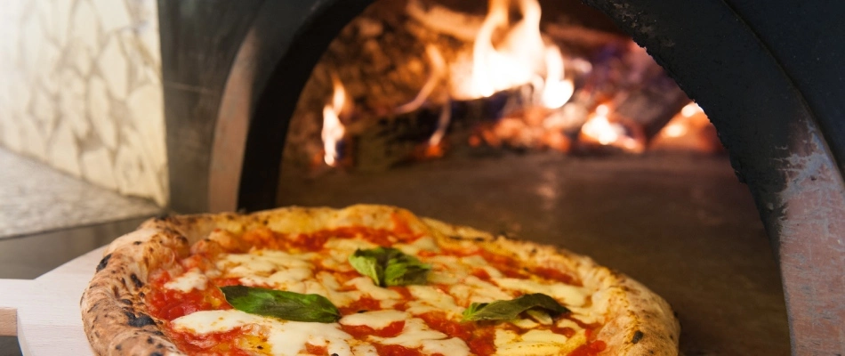 Pizza coming out from a pizza oven installed with outdoor kitchen in Grimes, IA.