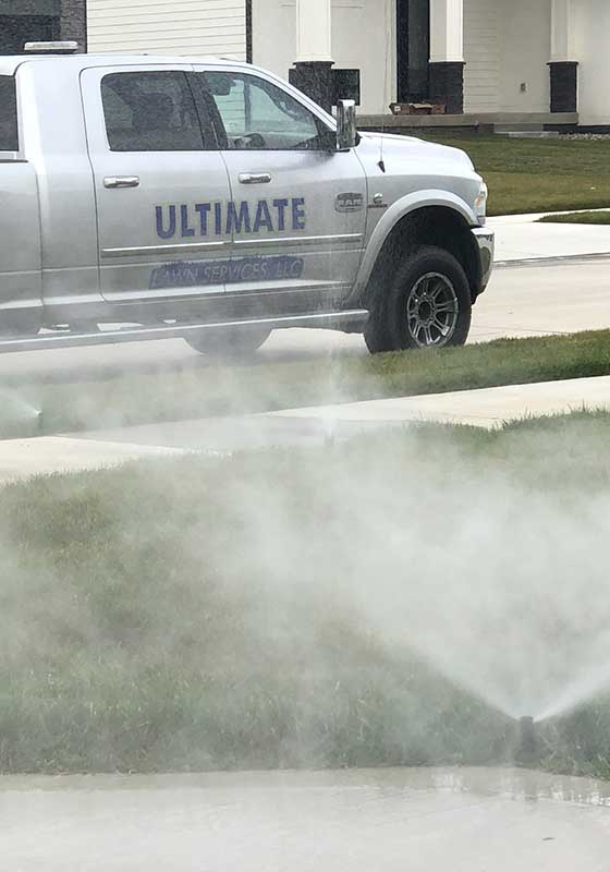 Ultimate Lawn Services work truck behind sprinklers in a yard outside Grimes, IA.